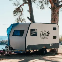 Przyczepa kempingowa nad morzem, z napisem "I Love TRAVEL". Zastanawiasz się, ile kosztuje przegląd techniczny przyczepy kempingowej?