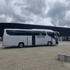Biały autokar firmy Eurotrans z otwartymi drzwiami stoi na placu przed nowoczesnym budynkiem.