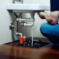 Hydraulik pracuje pod umywalką, rozwiązując problem, czym udrożnić rury odpływowe.