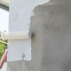 Wałek maluje białą farbą beton architektoniczny. Zastanawiasz się, czym pomalować beton architektoniczny? Oto odpowiedź!