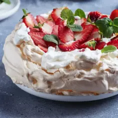 Pyszny tort bezowy z mascarpone i bitą śmietaną, ozdobiony świeżymi truskawkami i miętą.
