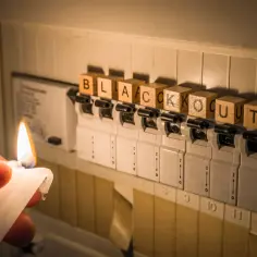 Płonąca świeca obok bezpieczników z literami "BLACKOUT" symbolizuje brak energii.