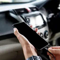 Dłoń podłącza telefon do radia samochodowego przez USB, aby odtworzyć muzykę.