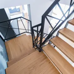 Nowoczesne schody metalowe z drewnianymi stopniami i czarną, geometryczną balustradą.