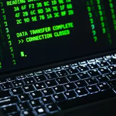 Zielony tekst na ekranie laptopa, "DATA TRANSFER COMPLETE >> CONNECTION CLOSED", sugeruje zakończenie operacji, być może związanej z szyfrowaniem BitLocker.
