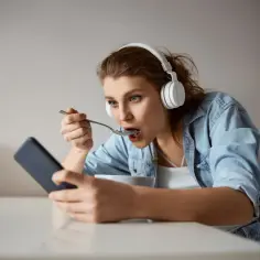 Młoda kobieta w słuchawkach je płatki, patrząc w telefon. Czy to objaw fonoholizmu?