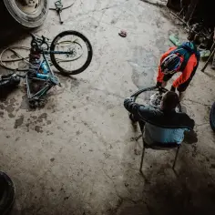 Przygotowania do rajdu rowerowego. Dwóch mężczyzn naprawia rower w garażu, otoczeni oponami i narzędziami.