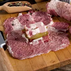 Przygotowanie zrazów z karkówki: rozbite plastry mięsa z boczkiem, ogórkiem i cebulą, obok nóż i przyprawy.