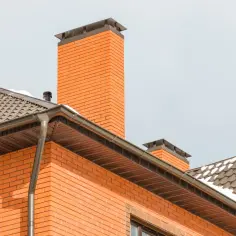 Ceglany komin i dach z rynnami. Pomysł na to, jak obudować komin wewnątrz domu, może inspirować się estetyką tej bryły.