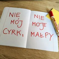 Otwarty zeszyt z zapisanymi czerwonym markerem polskimi idiomami: "Nie mój cyrk, moje małpy".