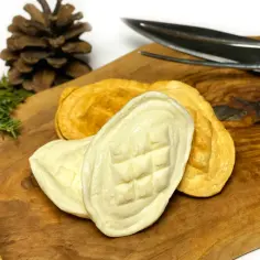 Oscypek na desce z drewna oliwnego, obok szyszki i gałązki iglastej.