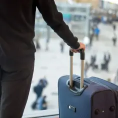 Mężczyzna z walizką w ręku, zastanawia się, czy pracownik może odmówić wyjazdu w delegację bez podania przyczyny. Tłum ludzi w tle.