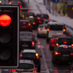 Czerwone światło sygnalizatora, a za nim sznur samochodów stojących w korku. Niektórzy kierowcy ignorują zakaz, ryzykując przejazd na czerwonym świetle.