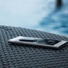 Smartfon z kroplami wody na ekranie, leżący na plecionej powierzchni. Dowód, że IP68 co oznacza: odporność na zanurzenie.