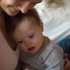 Ciepły uścisk mamy dla dziecka z trisomią 21. Ich spojrzenia pełne miłości.