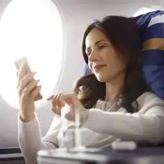 Kobieta w samolocie korzysta z telefonu, sprawdzając, czy w samolocie jest wifi.