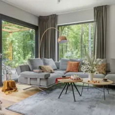 Nowoczesny salon z szarą sofą, stolikami kawowymi i widokiem na las. Inspiracja, jak urządzić salon, by był przytulny i stylowy.