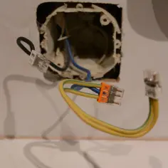 Jak podłączyć kabel dwużyłowy do wtyczki z bolcem? Widoczne złączki elektryczne i przewody w puszce instalacyjnej.