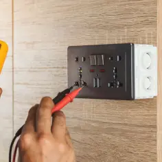 Elektryk sprawdza napięcie w gniazdku za pomocą miernika. Oto jak zmierzyć miernikiem baterie, lub napięcie w sieci.