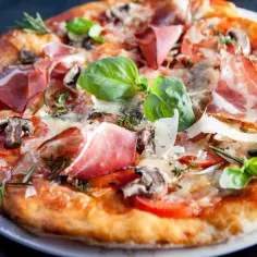 Pyszna pizza z szynką parmeńską, pieczarkami i bazylią. Widać, jak powstaje pizza, gdy składniki łączą się w idealną całość.
