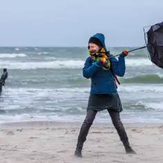 Dziewczynka walczy z wiatrem na plaży, próbując utrzymać parasolkę. Czy to znak, że zbliża się sztorm na Bałtyku?