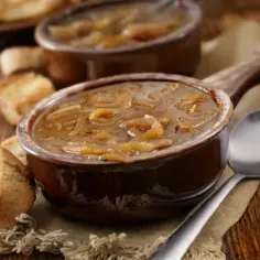 Zupa cebulowa w brązowej miseczce z grzankami i łyżką na drewnianym stole.