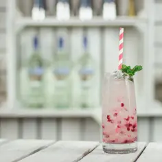 Orzeźwiający drink z granatem i miętą, idealny na toast "cin cin". Na półce w tle widać butelki alkoholu.