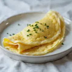 Złożony, gładki francuski omlet z posiekanym szczypiorkiem na talerzu.