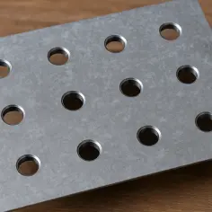 Metalowa płytka z rzędem otworów na drewnianym tle.