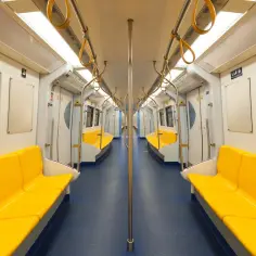 Wnętrze pustego wagonu metra z żółtymi siedzeniami i poręczami.