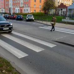 Kobieta z paczką przechodzi przez przejście dla pieszych. Samochód zatrzymał się, by ją przepuścić.