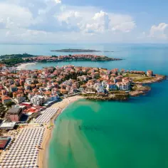 Widok z lotu ptaka na bułgarskie miasteczko z czerwonymi dachami, plażę z leżakami i turkusowe morze.