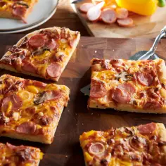 Kawałki pysznej pizzy z kiełbasą, pieczarkami i papryką na drewnianej desce.