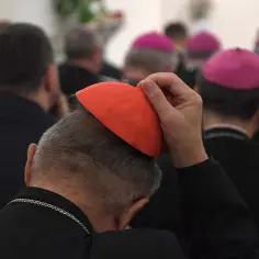 Biskupi w różowych biretach i jeden z czerwoną piuską, dyskutują o przyszłości funduszu kościelnego.