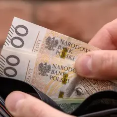 Dłoń wkłada banknoty 100 zł do portfela. To może być część oszczędności na trzynasta emerytura 2026.