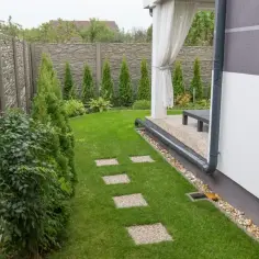Nowy system odprowadzenia wody z rynien na trawnik, z kamiennym chodnikiem i zielonym ogrodem.