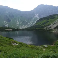 Ciemne jezioro górskie otoczone zielonymi zboczami i skalistymi szczytami.