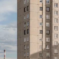 Szary blok mieszkalny z wieloma oknami na tle błękitnego nieba z chmurami.