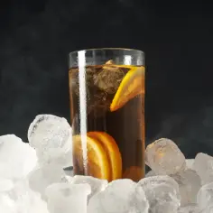 Szklanka long drink z lodem i cytryną, otoczona bryłami lodu, tworzy chłodny klimat. Zbyt duża ilość lodu może szybko rozcieńczyć napój.