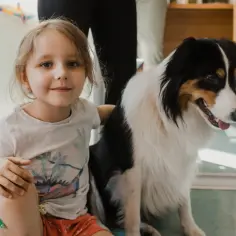 Uśmiechnięta dziewczynka i jej przyjaciel border collie siedzą razem.