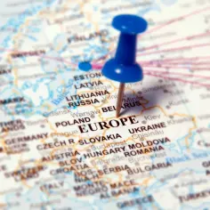 Mapa Europy z pinezką wbita w słowo "EUROPE". Widoczne stolice krajów Europy, takie jak Warszawa, Praga, Wiedeń, Budapeszt, Kijów.