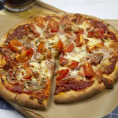 Pyszna pizza z szynką i pieczarkami, z pomidorkami i ciągnącym serem, gotowa do podania.