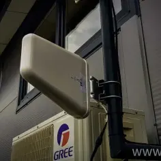Antena LTE zamontowana na ścianie budynku, obok jednostki klimatyzacyjnej. Dowiedz się, jak ustawić antenę LTE Plus dla lepszego zasięgu.