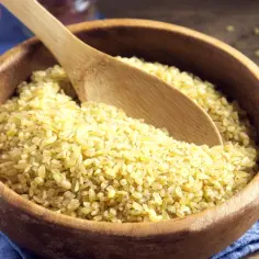 Drewniana miska pełna kaszy bulgur z drewnianą łyżką.
