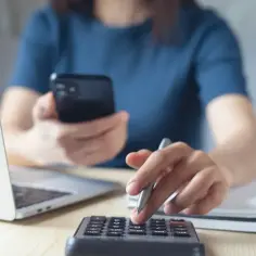 Kobieta z telefonem i kalkulatorem liczy staż pracy, uwzględniając okres pobierania zasiłku dla bezrobotnych.