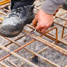 Dłoń pracownika wiąże zbrojenie budowlane drutem.