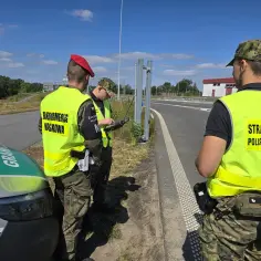 Strażnicy graniczni w kamizelkach odblaskowych sprawdzają dokumenty przy granicy państwowej.