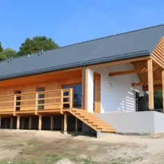 Nowoczesny domek fiński z drewnianym tarasem i okapem, otoczony zielenią.