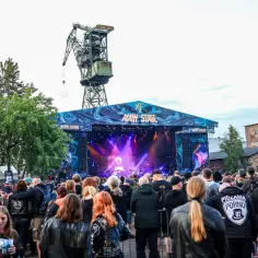 Tłum fanów na festiwalu Mystic Festival w Gdańsku. W tle scena z napisem "Main Stage" i zabytkowy dźwig. Wiele takich festiwali w Polsce przyciąga miłośników muzyki.