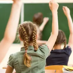 Uczniowie z podniesionymi rękami, ciekawi lekcji. Czyżby to był moment, od której klasy drugi język obcy?